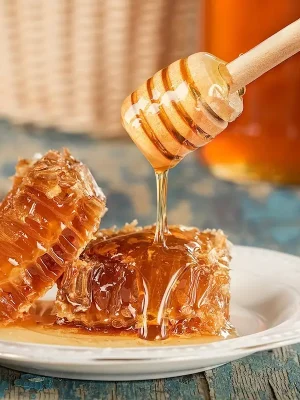  Honiglöffel aus Holz mit Honig über Honigwabe